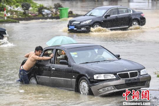 6月13日，惠州惠東縣新平大道上，市民在雨中推行拋錨的車輛?！￡愺K旻 攝